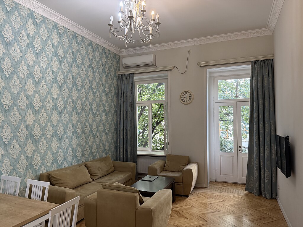 Wohnzimmer der Ferienwohnung mit hellblauer Ornamenttapete, Kronleuchter und Fischgrätparkett