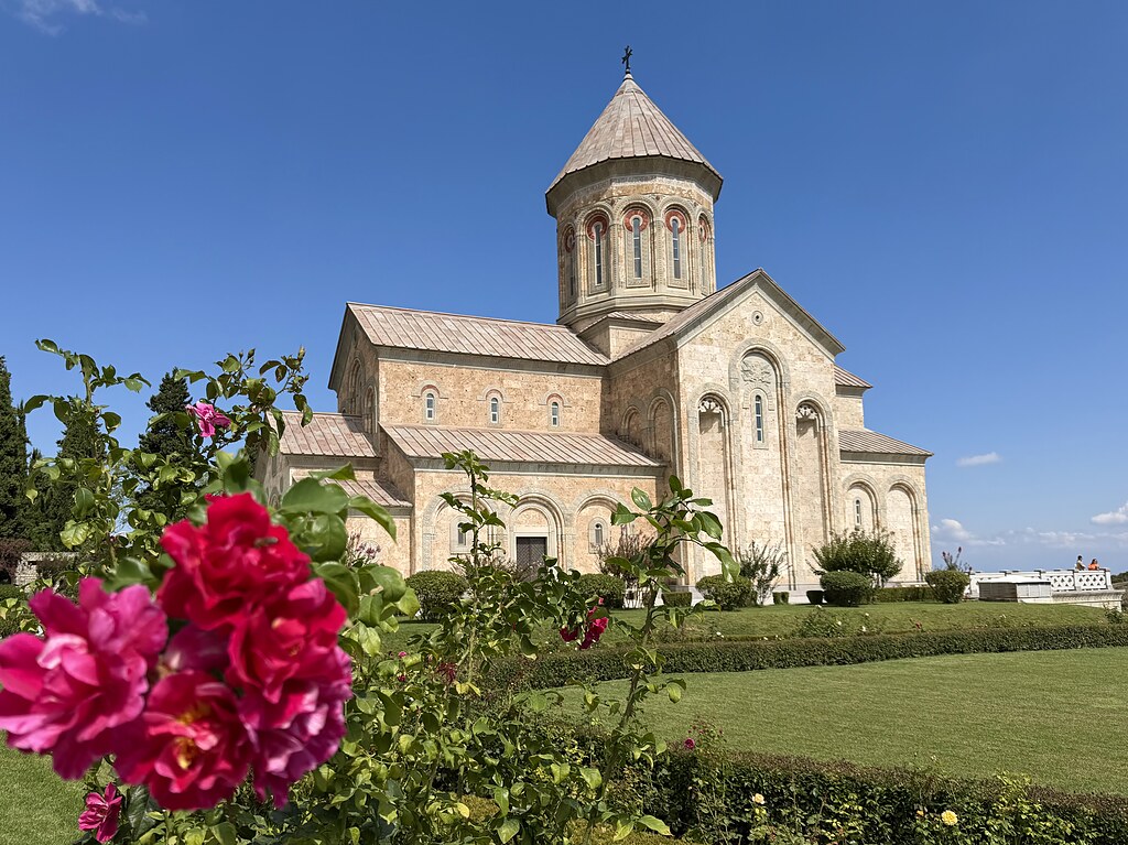 Frauenkloster Bodbe umgeben von grünen Bäumen, Wiesen, Hecken, rosanen Rosen und blauem Himmel