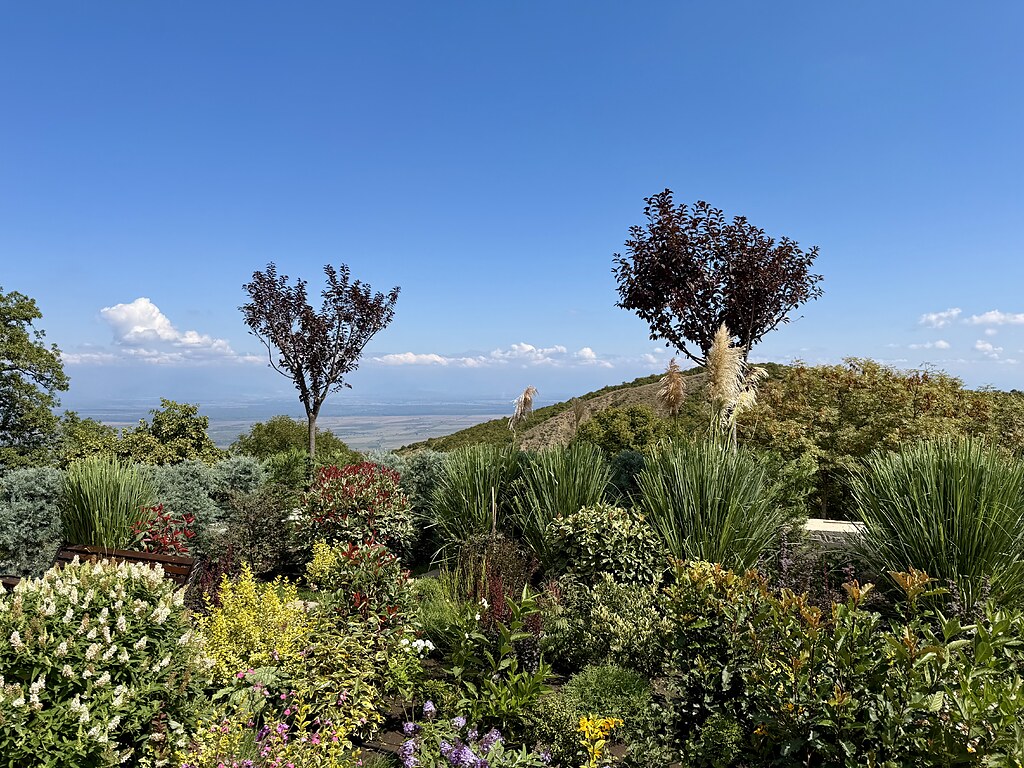 schön angelegte Beete beim Kloster Bodbe, viele bunte Blumen, Bäume mit roten Blättern, Blauer Himmel und Blick auf einen Hügel und ins Tal.
