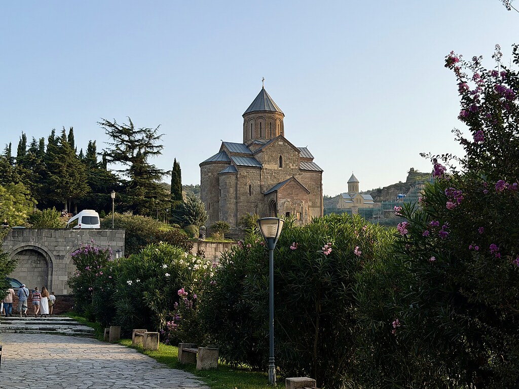 zwei Kathedralen, jeweils auf einem Berg in Tiflis, darum eine angelegte Grünfläche mit blühenden Büschen.