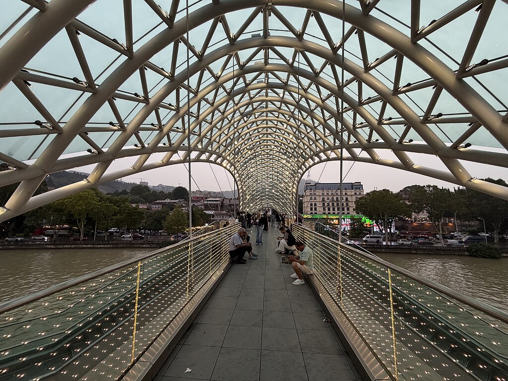 Friedensbrücke Tiflis über den Fluss Kura. Es sitzen Menschen auf der Brücke