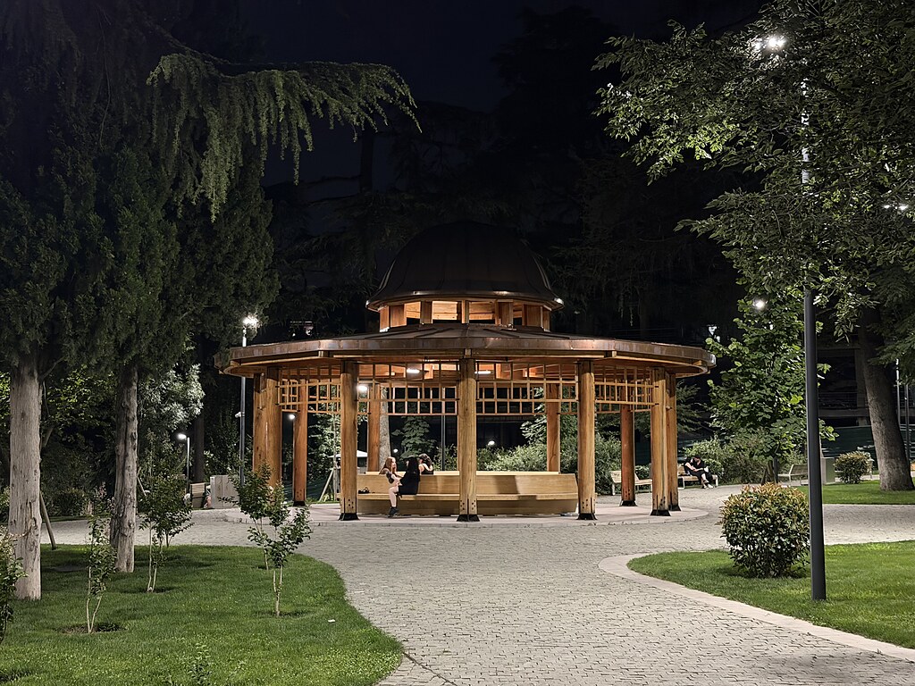 Rundes Holzdach mit Säulen im Vera Park, Tiflis, Georgien. Daneben leuchten Laternen.