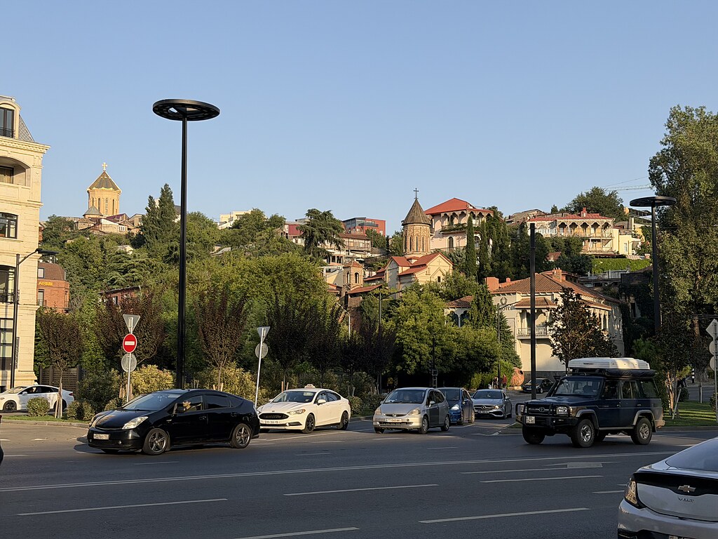 Hang mit alten Gebäuden in Tiflis, davor eine mehrspurige Straße mit Autos.