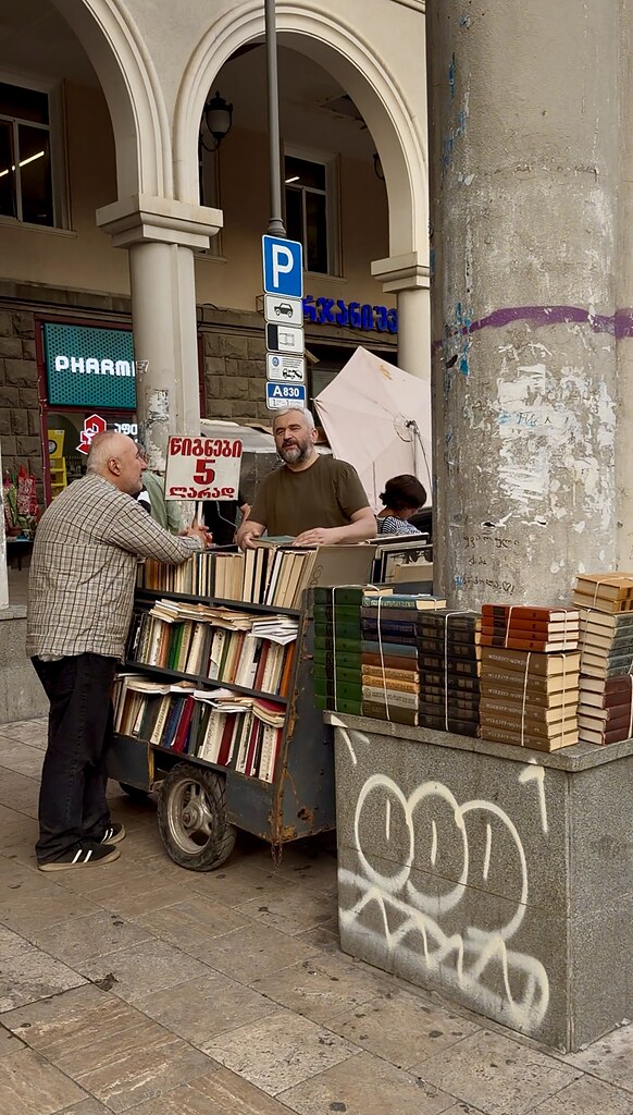 Zwei Männer unterhalten sich an einem Bücherstand, der auf einem Bürgersteig aufgebaut wurde.