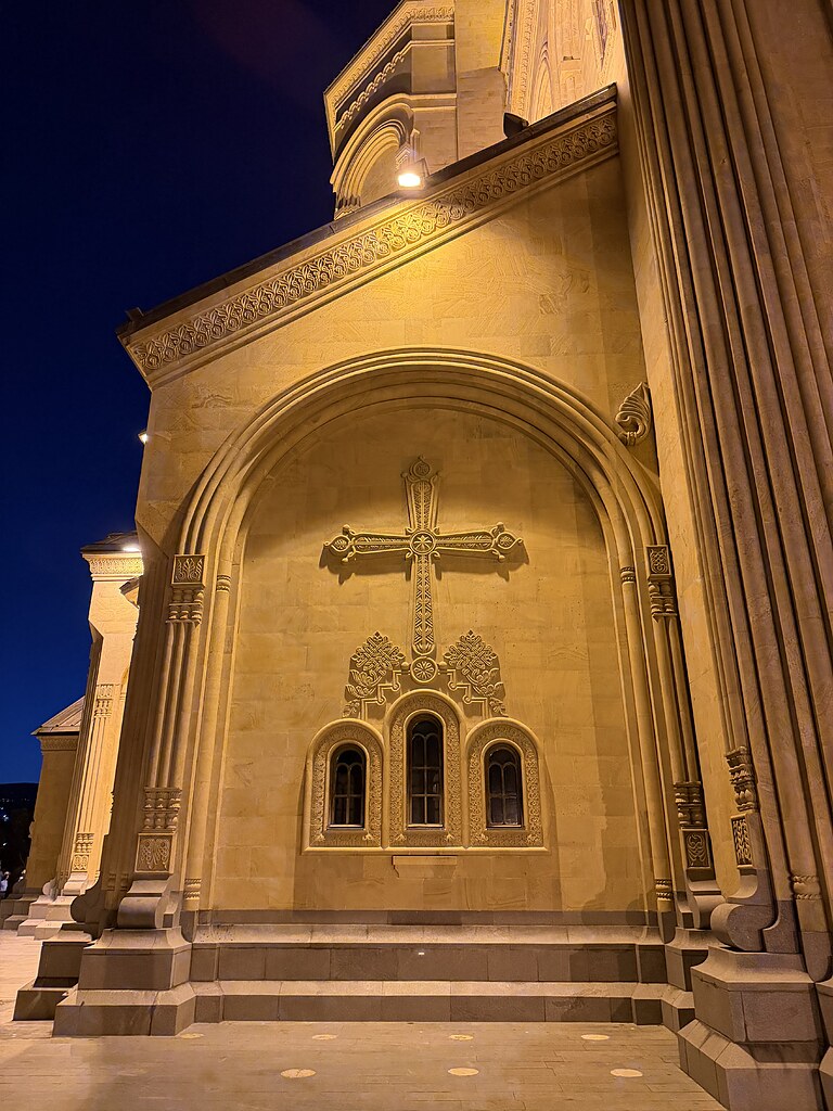 Ein verziertes Kreuz an der Fassade der Sameba-Kathedrale, darunter drei Fanster, beleuchtet in Tiflis