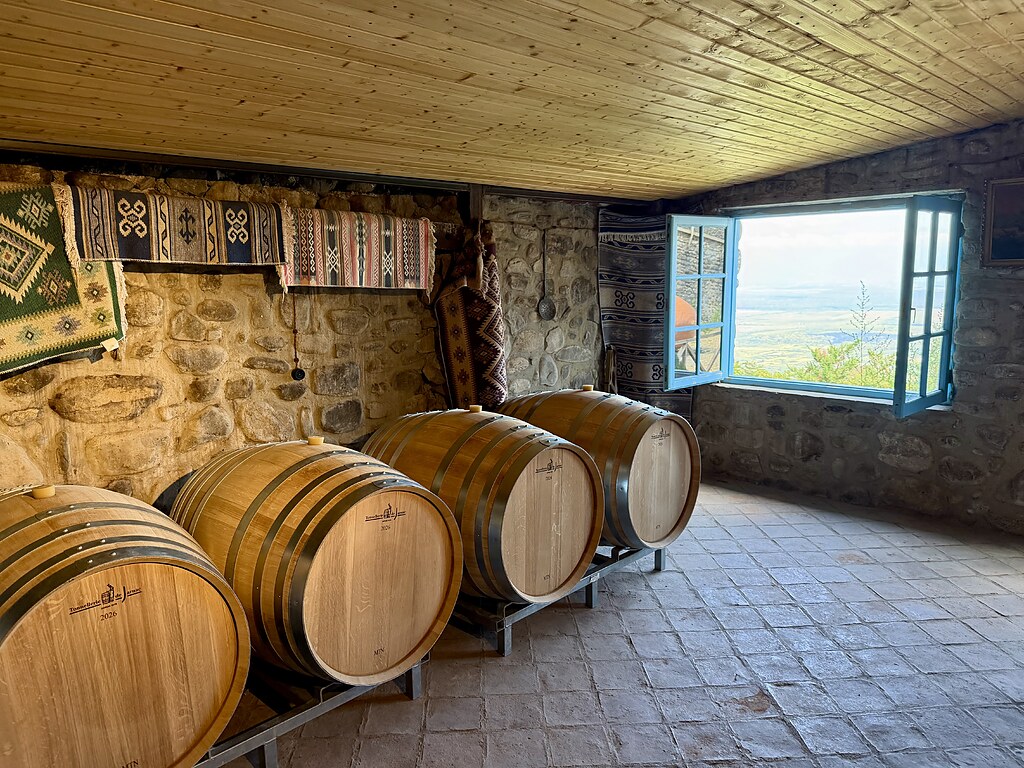 Weinfässer aus Holz auf dem Boden im Weinkeller, neben einem hellblauen offenen Fenster