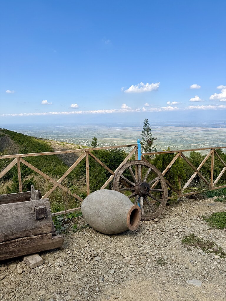 Georgisches Weinfass aus Ton neben einem Holzrad im Garten