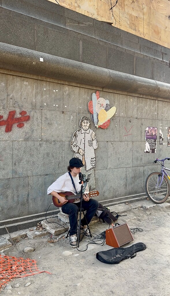 Straßenmusiker in Tiflis mit einer Gitarre in einer Baustelle vor einem Mosaik
