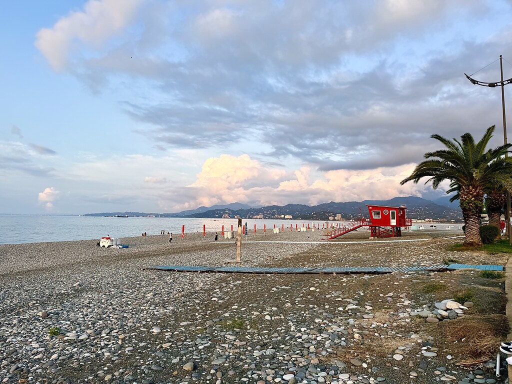 Strand mit Steinen und Palmen am Schwarzen Meer in Batumi, Georgien mit Bergpanorama.