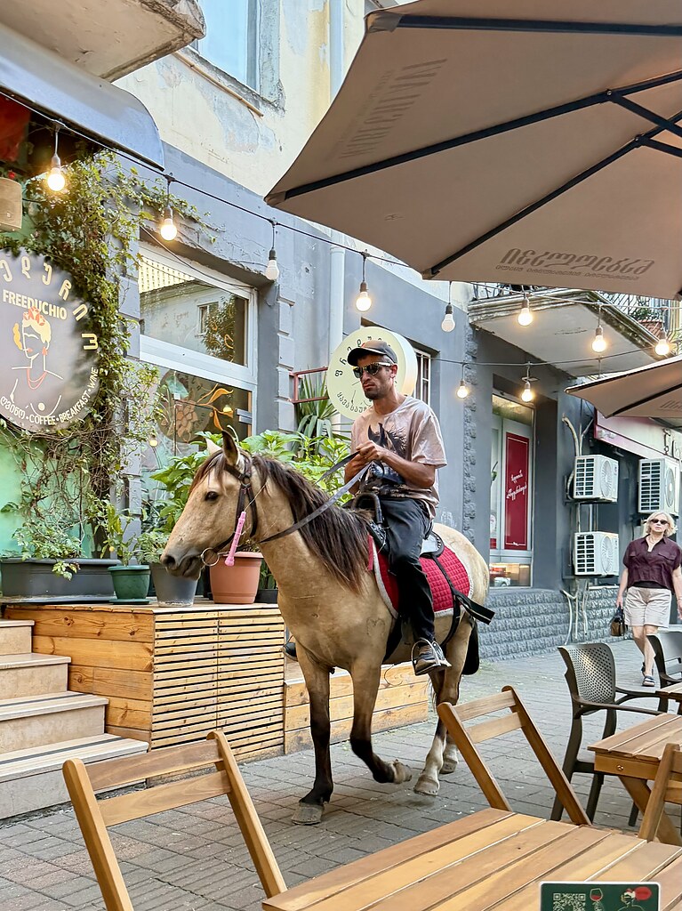 Ein Mann reitet auf einem Pferd auf dem Bürgersteig an einem Restaurant vorbei in Batumi, Georgien.