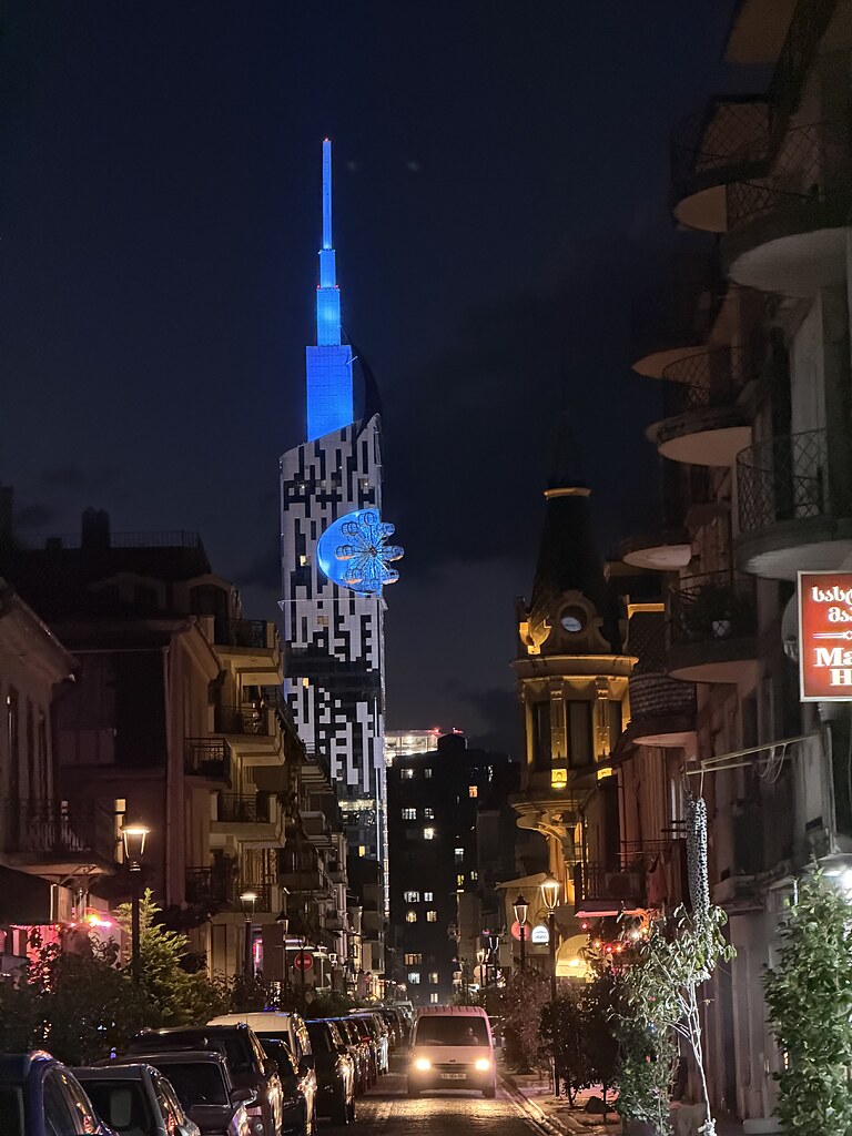 Batumi Tower, Hochhaus mit Riesenrad am Ende einer beleuchteten Straße in der Altstadt von Batumi, Georgien am Schwarzen Meer.
